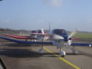 Three Robin DR400 aircraft in a row on a EHRD taxiway. A fourth airplane is seen in the background.